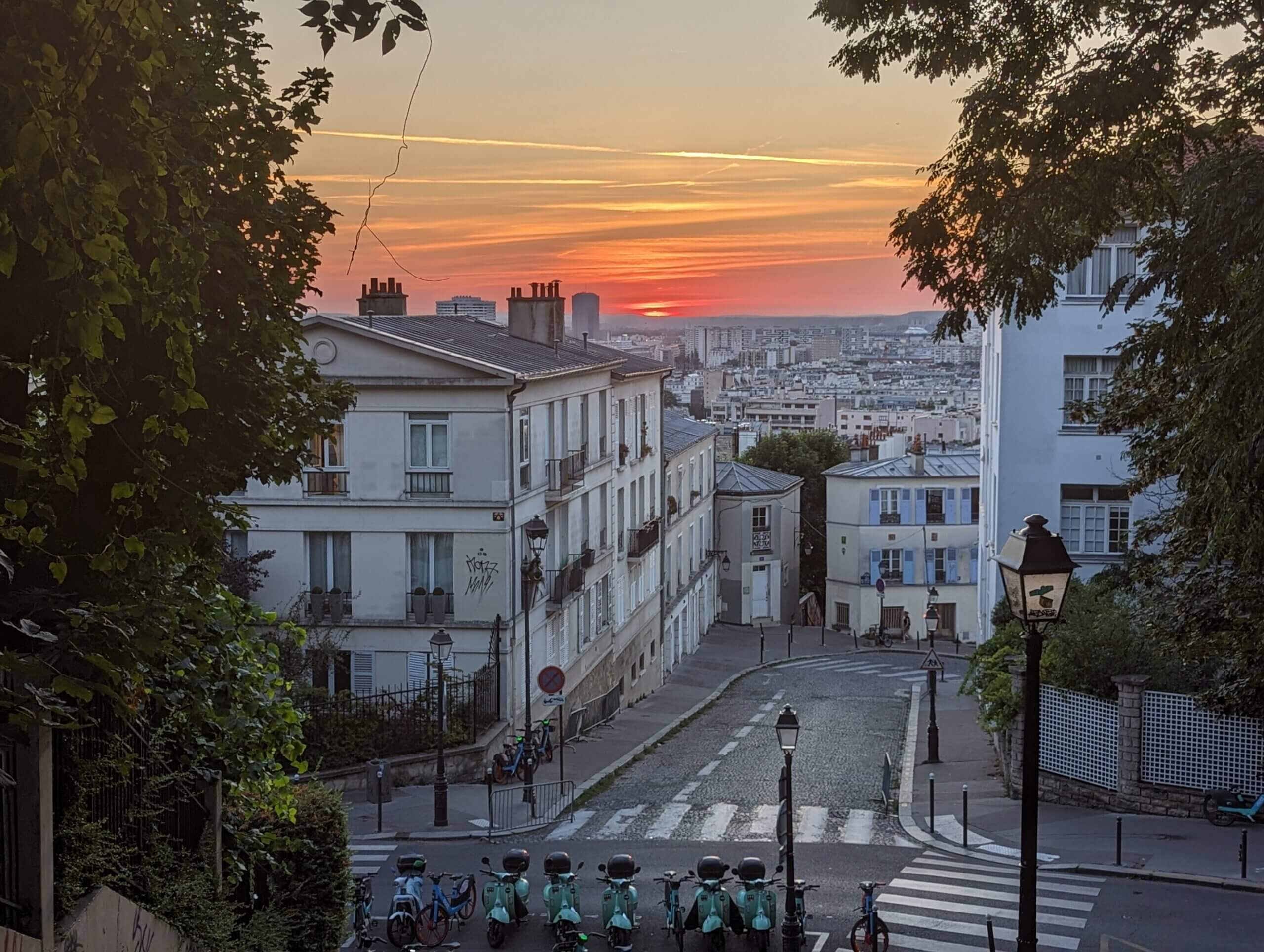 A rich, golden sunrise stretching behind white town houses in Montmatre in Paris, France.